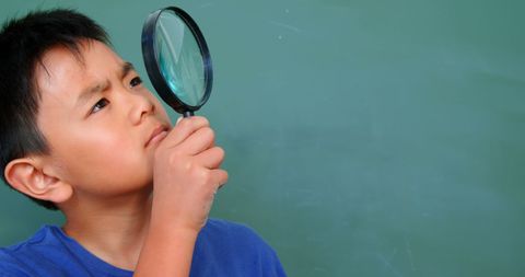 Curious schoolboy exploring with magnifying glass in classroom