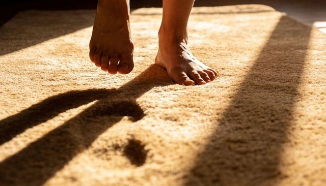 Sunlit bare feet stepping on plush beige carpet casting long warm shadows evoking cozy home comfort