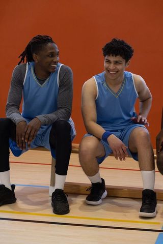 Smiling Teammates in Blue Jerseys Sitting on Basketball Court Bench