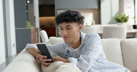 Young Man Relaxing on Modern Sofa Using Smartphone in Stylish Living Room