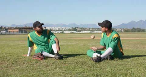Male Baseball Teammates Relaxing and Tossing Ball on Field Wearing Green Yellow Uniforms