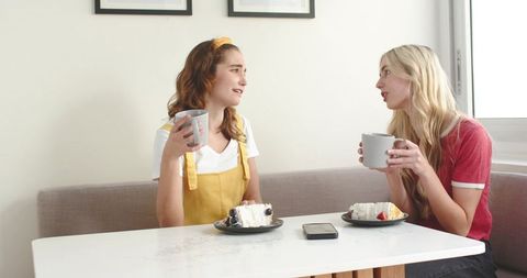 Two friends chatting over coffee and cake in cozy kitchen nook