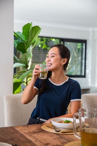 Smiling young woman enjoying refreshing drink at cozy dining table