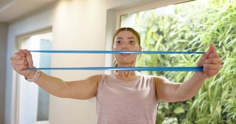 Young woman performing resistance band chest opener workout in bright home gym