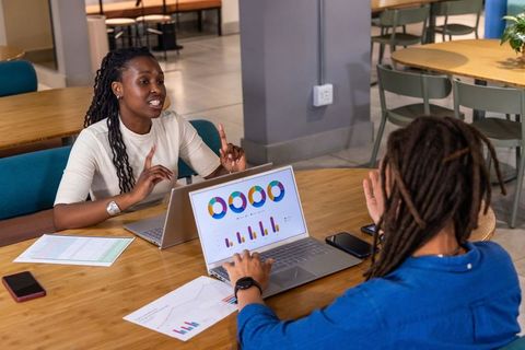 African American women collaborating on analytics dashboards and charts on laptops