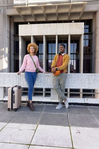 African american friends leaning on concrete balustrade holding basketball and suitcase