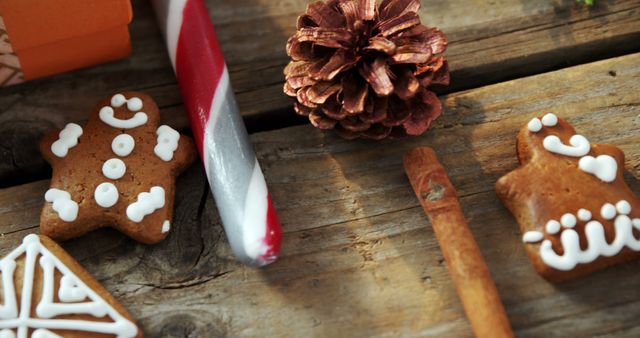 Holiday-themed treats and decorations are arranged on a wooden surface, featuring gingerbread cookies, a candy cane, cinnamon stick, and a pine cone. Capturing the essence of festive celebrations, the image evokes the warmth and sweetness of the holiday season.