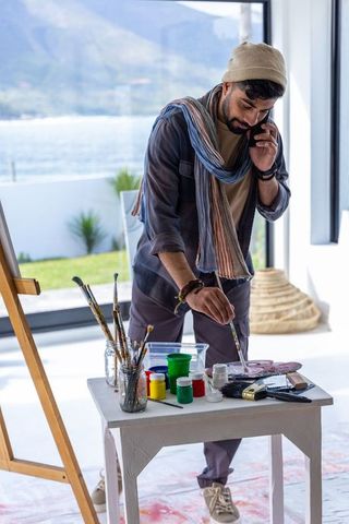 Man talking on phone while painting in bright coastal studio