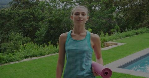 Focused Young Woman Holding Pink Yoga Mat Outdoors By Pool