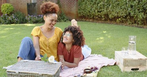 African american friends enjoying relaxed backyard picnic on blanket with wicker basket