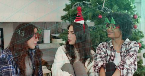 Friends wearing festive headbands and glasses sitting by christmas tree in cozy room
