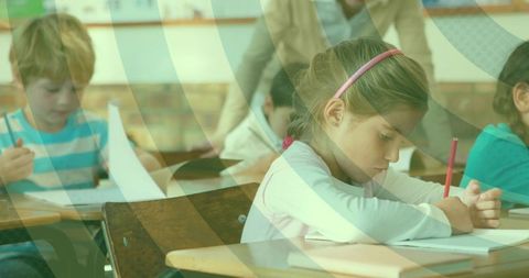 Elementary girl writing and concentrating on worksheet at wooden desk wearing pink headband