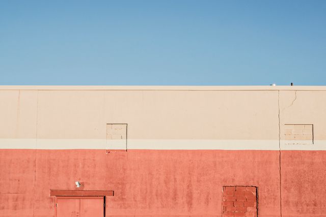 This image showcases a minimalist perspective of a textured building wall under a clear blue sky. The simplicity and clear composition make it suitable for use in architectural designs, urban development presentations, or minimalist art applications. Perfect for backgrounds or editorial features focusing on structural design and modern urban elements.
