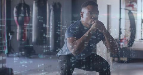 Focused black athlete squatting in boxing gym with futuristic data overlay for training