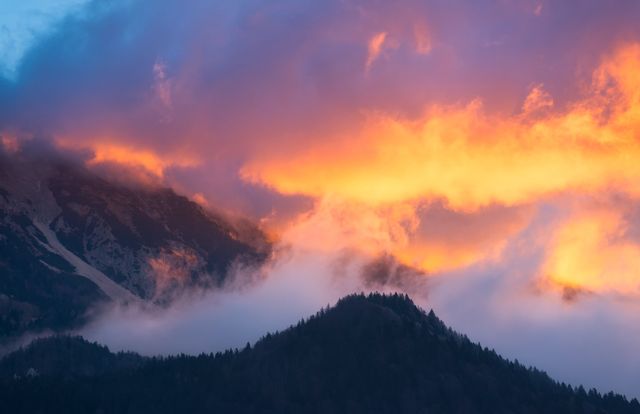 Dramatic scene capturing mountain tips glowing at sunrise. Fog drifts across landscape partially hiding forested peaks. Spectacular vibrant sky with a palette of warm colors suggests breathtaking views. Perfect for travel blogs, nature magazines, posters, and calendars evoking a sense of tranquility and awe.