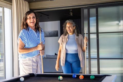 Diverse women laughing and playing pool in bright modern home leisure room