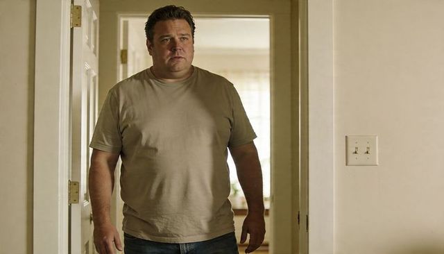 Thoughtful adult male standing in doorway wearing beige t-shirt and jeans, sunlit interior