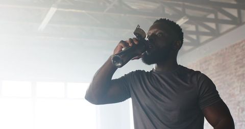 Athletic Man Enjoying Refreshing Drink After Workout in Industrial Gym