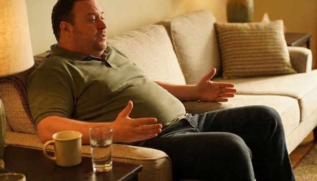 Man relaxing and conversing on beige sofa, casual home living room, warm ambient light