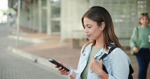 Young woman checking smartphone while waiting at urban transit stop with backpack