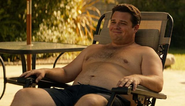 Relaxing shirtless man on sunlit backyard lounger wearing wedding band and swim shorts