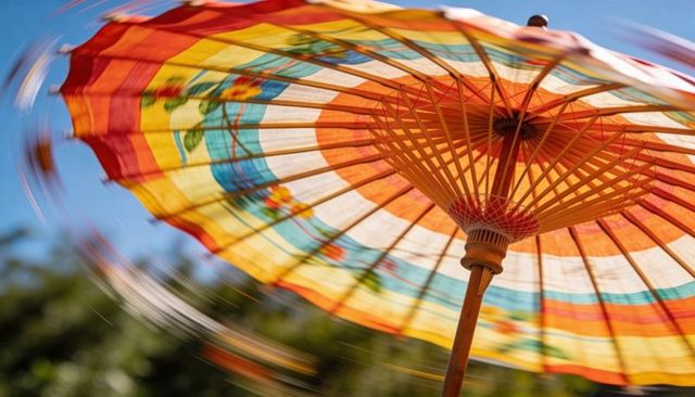 Colorful spinning paper parasol with floral pattern and wooden ribs against blue sky