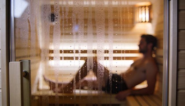 Male Relaxing in Wooden Sauna Through Fogged Glass with Warm Amber Lighting