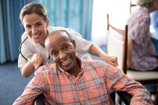 This image shows a cheerful female doctor standing behind a smiling senior man in a wheelchair at a retirement home. It can be used for promoting healthcare services, elderly care facilities, medical support, and senior living communities. Ideal for websites, brochures, and advertisements related to healthcare and senior care.