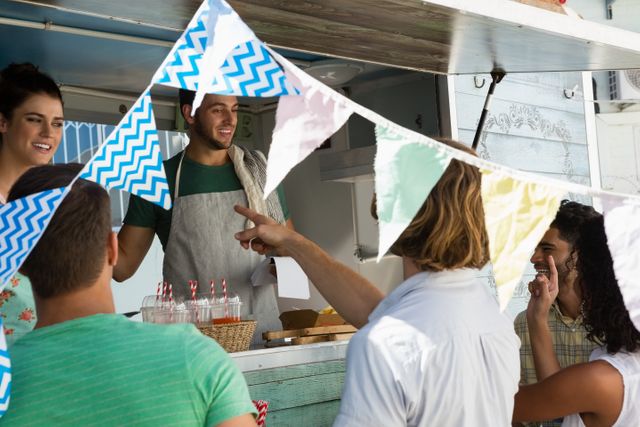 Group of friends enjoying food and drinks at an outdoor food truck. Colorful bunting adds a festive atmosphere. Ideal for use in marketing materials for food festivals, community events, or urban lifestyle promotions.