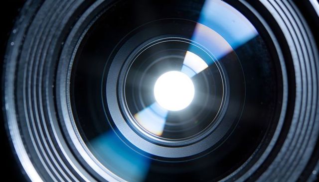 Macro close-up camera lens showing glowing aperture blades with blue reflection flare