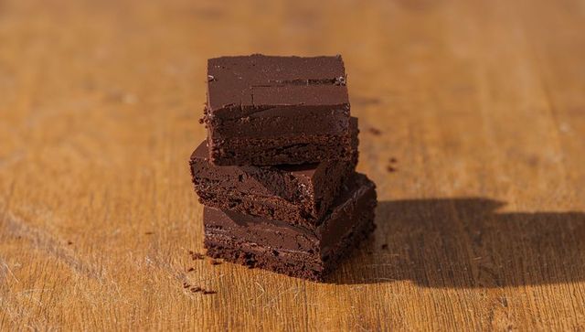 Decadent dark chocolate squares stacking on rustic wooden board with crumbs