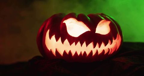 Grinning jack-o'-lantern with jagged teeth glowing orange and green fog backlight