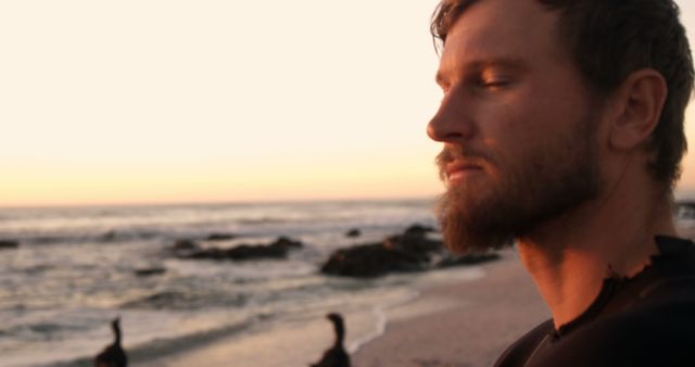Happy caucasian man with beard relaxing on beach with closed eyes at sundown, copy space. Tranquility, meditation, free time, travel, nature and healthy outdoor lifestyle, unaltered.