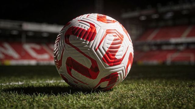 Resting white soccer ball with red textured panels on illuminated stadium pitch at night