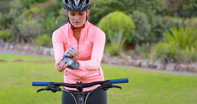 Young woman preparing for cycling in a park, wearing protective gear including helmet and gloves. Ideal for advertisements or articles on fitness, active lifestyle, and outdoor sports. Useful for health and wellness campaigns, cycling safety materials or promotional content for sports apparel.