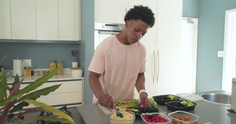 African american man preparing healthy meal-prep bowls on modern kitchen island