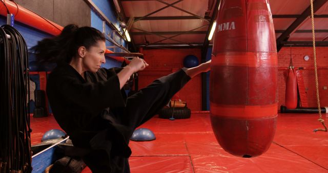 Woman practicing a high kick technique in a martial arts gym. This scene can be useful for articles, blogs, and advertisements about fitness routines, self-defense classes, martial arts training, perseverance, empowerment, and healthy lifestyles.