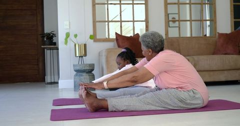 African american grandmother stretching with granddaughter on yoga mats at home
