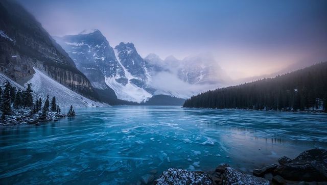Frozen turquoise alpine lake stretching through misty mountain valley, ice floes at dawn