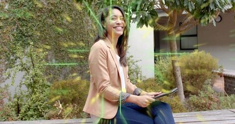 Asian professional woman smiling and holding tablet while sitting on courtyard bench