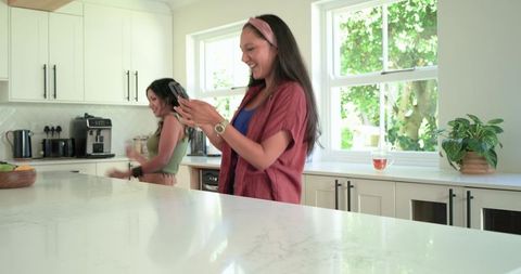Smiling woman using smartphone in bright modern kitchen with marble island and friend