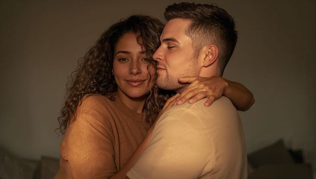 Couple embracing on sofa at golden hour, warm intimate moment, ring catching light