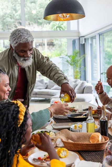 African american multigenerational family sharing dinner with grandfather pouring olive oil