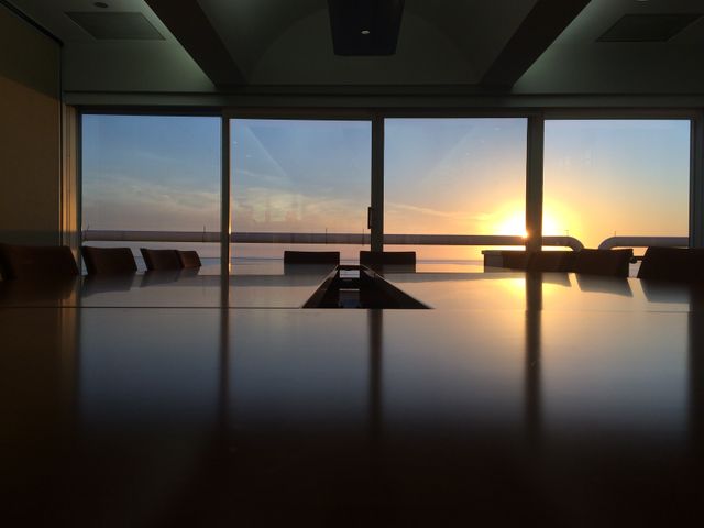 This image depicts an empty conference room featuring large windows that provide a stunning sunset view. Perfect for illustrating serene and modern office environments, business settings, or corporate situations. An ideal visual for business websites, corporate videos, or promotional materials emphasizing a sophisticated and tranquil workplace.