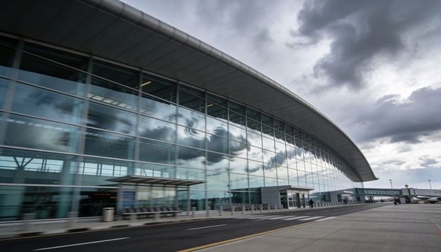 Modern curved airport terminal reflecting storm clouds on glass facade at curbside