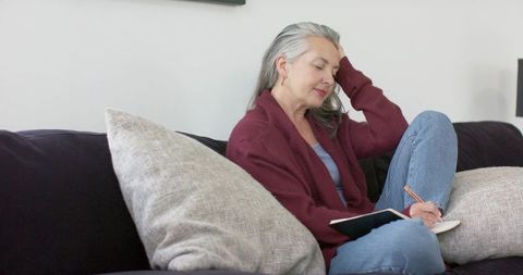 Mature woman writing journal on couch during quiet reflective moment in cozy living room