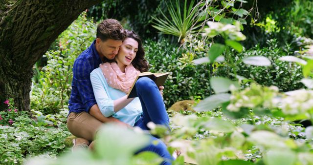 Couple enjoying each other's company while reading book in a lush green garden. Ideal for themes around romance, relaxation, nature, and togetherness. Perfect for use in articles promoting bonding activities for couples, nature retreats, or relaxing pastimes. Can also be used for book clubs or reading-related content.
