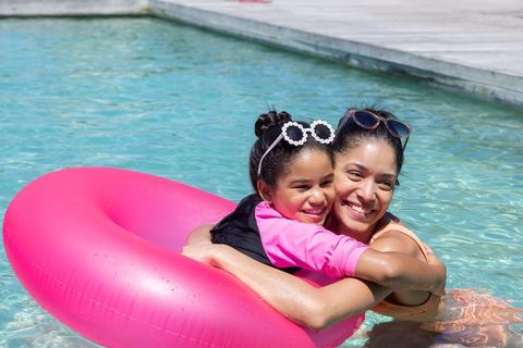 African american mother and daughter hugging on bright pink inflatable ring in sunny pool