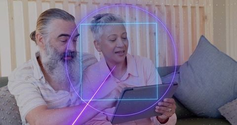 Older couple browsing tablet with neon ar overlay while sitting on cozy living room couch