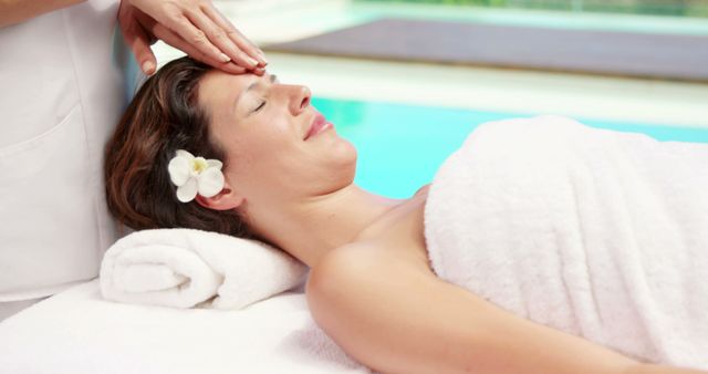 This portrays a tranquil scene featuring a woman enjoying a spa treatment near a pool. She has a flower in her hair and appears to be relaxed. Ideal for use in wellness and beauty promotions, spa advertisements, or relaxation-themed content.
